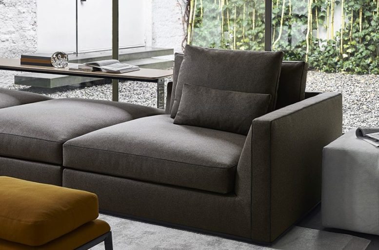 Particolare del divano  Richard in tessuto, dotato di doppi cuscini per garantire comfort nella seduta. Sullo sfondo la consolle Eileen con piano in legno.