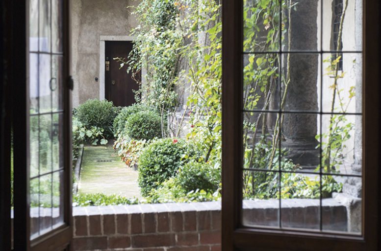 La porta vetrata in legno massiccio si apre direttamente sotto il porticato nel chiostro a mostrare di fronte un arco rifilato in laterizio.