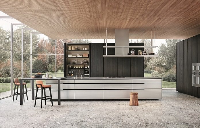 Cucina Phoenix, design R&D Poliform. Basi con ante, cassetti ed estrattori in acciaio e sagoma frontale laccato goffrato carbone, piano in acciaio KitchenAid con telaio di supporto laccato goffrato carbone. Cappa Factory a isola in acciaio. Colonne con ante in olmo nero e distanziatori verticali in laccato goffrato carbone. Piano snack Blade, design R&D Poliform, in olmo nero e sgabelli Ventura, design Jean-Marie Massaud, in olmo nero con seduta rivestita di pelle non sfoderabile Soft 4 cognac.