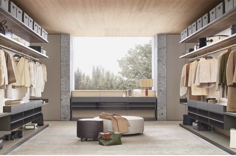 Cabina armadio Ubik, design R&D Poliform. Pannelli a parete e basamenti in nobilitato Skin laccato opaco 94 latte, con struttura e zoccolo in verniciato ardesia. Ripiani superiori in nobilitato rovere cenere con frontale verniciato ardesia e luce a led integrata. Sui ripiani più alti, scatole con coperchio rivestite in tessuto txt piombo. Tubi appendiabiti rivestiti in tecnopelle 05 latte. Cassettiere a vetrina sospese con piano superiore in vetro trasparente riflettente e vassoio estraibile con frontale verniciato ardesia, cassetti con frontali in vetro riflettente fumé, telaio verniciato ardesia e interni in tecnopelle 05 latte. Ripiani inferiori in tecnopelle 05 latte e telaio verniciato ardesia. Pouf New York, design Jean-Marie Massaud, uno rivestito in tessuto sfoderabile Skyros 02 sabbia, l’altro in pelle Soft 10 prugna, entrambi con piedini brown nickel lucido.