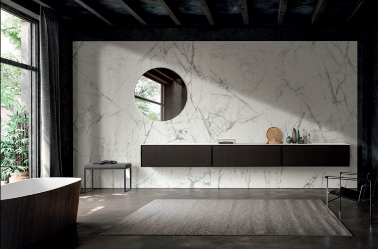 FRAME
Frame è un progetto dedicato ad un’area di gusto sofisticata, una rilettura raffinata delle forme classiche. Linee essenziali e rigorose vengono ammorbidite da una cornice che definisce e sottolinea il profilo dell’anta: la maniglia, accolta nel suo spessore, risulta incassata e nascosta alla vista. L’anta Frame con il suo telaio sp. 1 cm , dettaglio tecnico divenuto espressione formale, entra a far parte della collezione bagno Modulnova. Un ambiente emozionale caratterizzato dalla matericità delle essenze del legno rovere caffè, verniciato con oli naturali, e dalla presenza di una preziosa parete in gres effetto marmo.